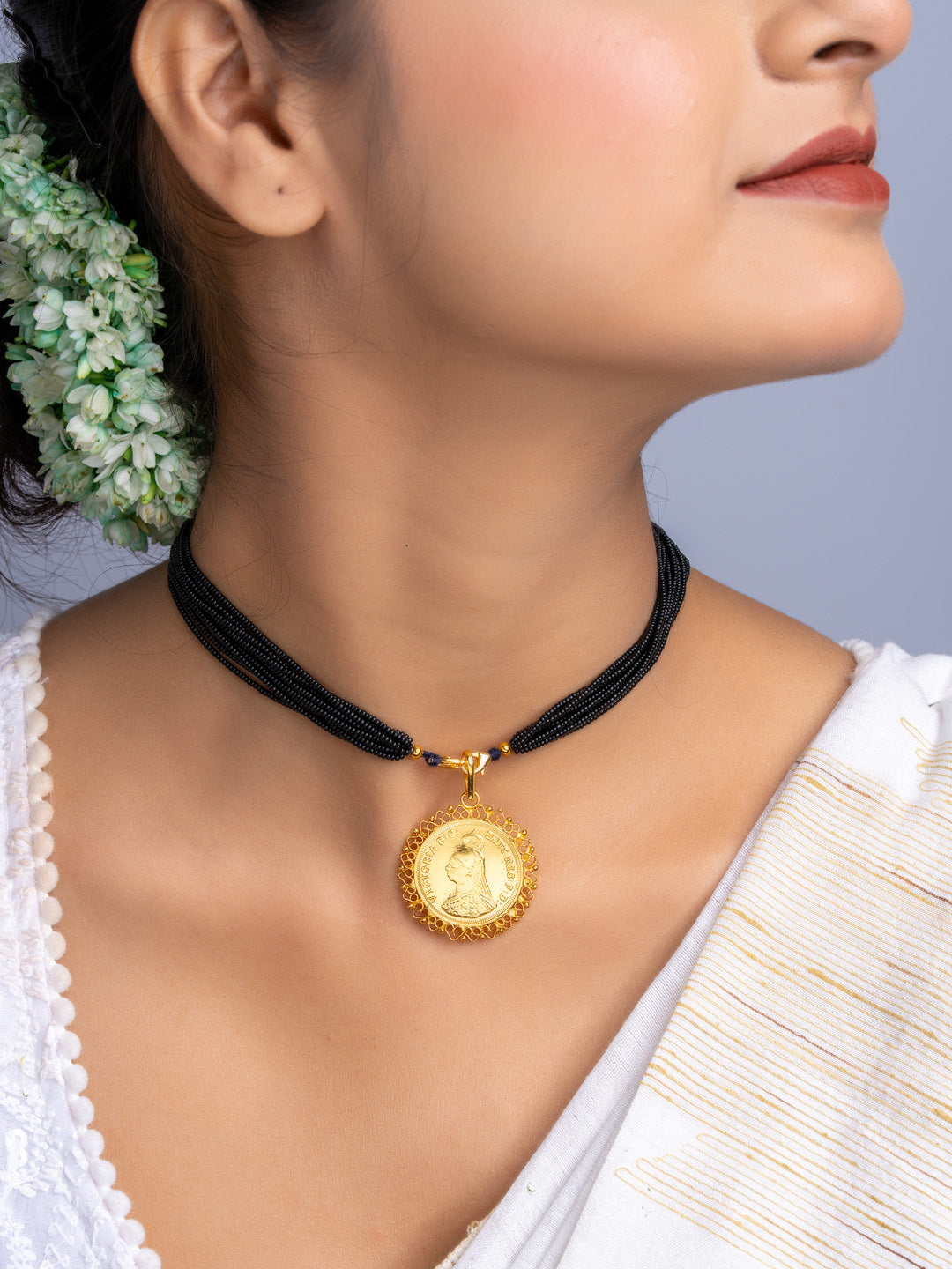 Gold plated pendant with black beaded necklace worn by woman with traditional attire