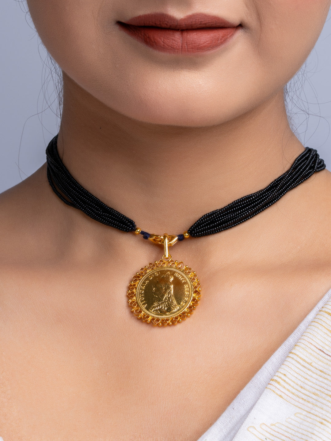 Gold plated pendant with intricate design on black beaded necklace worn around neck