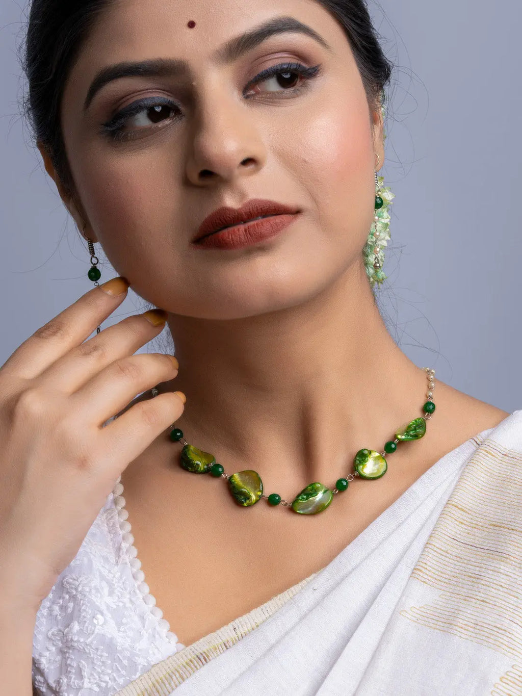 Handmade mother of pearl necklace set with green stones worn by woman in white saree
