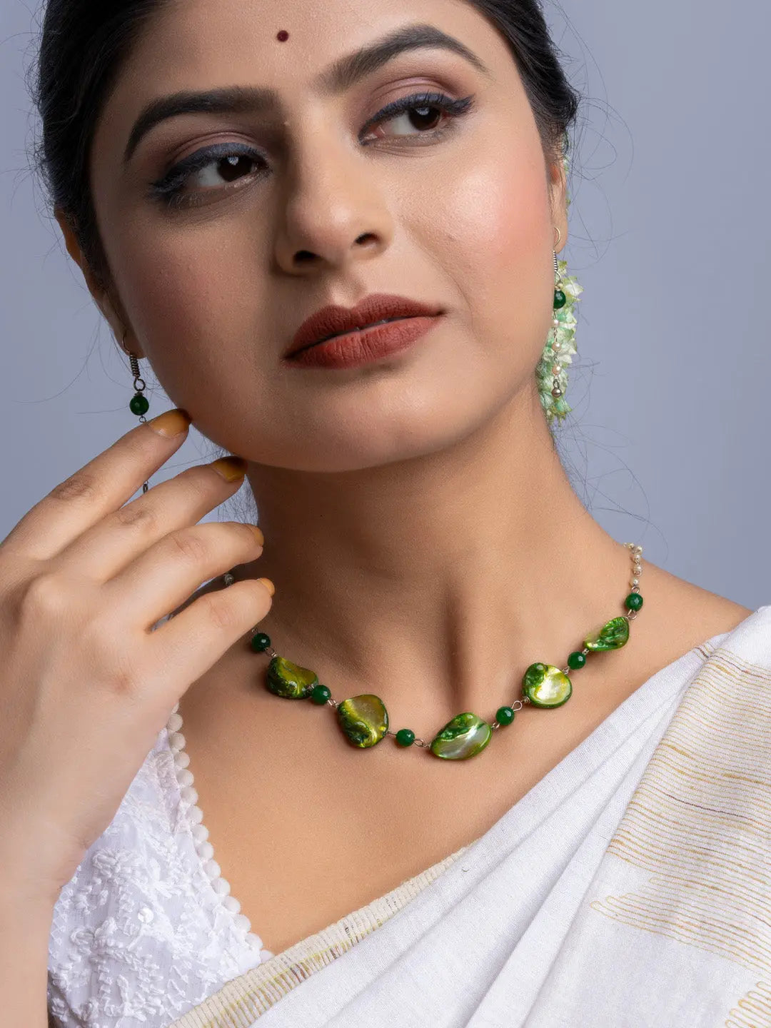 Handmade mother of pearl necklace set with green stones worn by woman in white saree