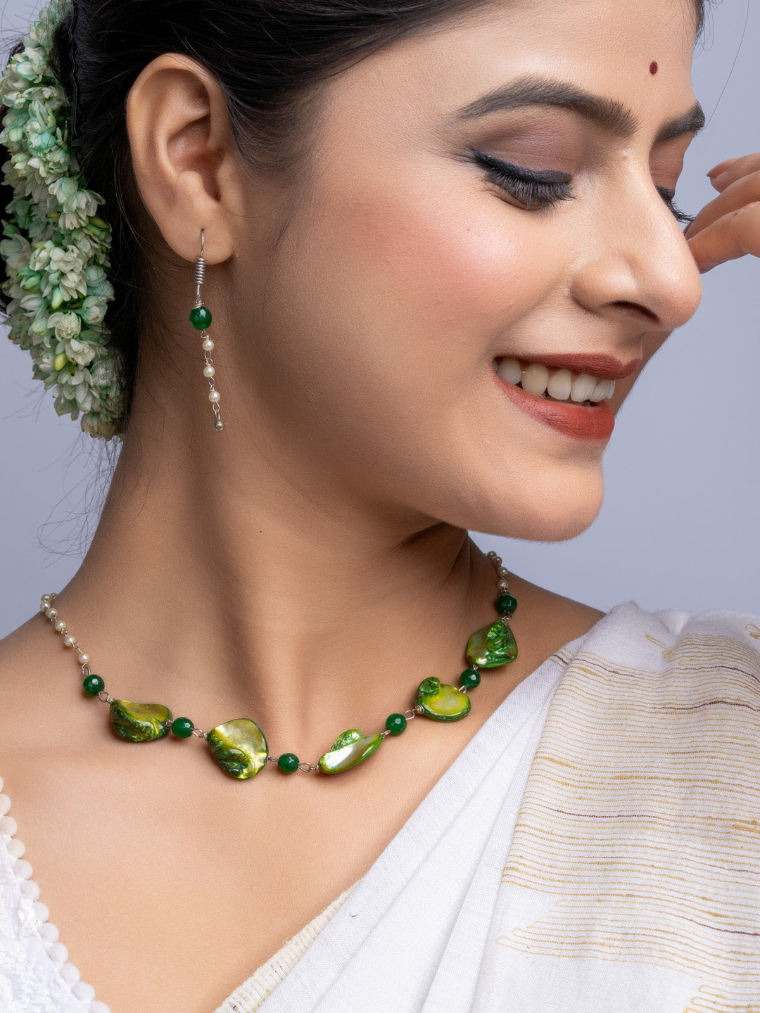 Handmade mother of pearl necklace set with green beads worn by woman smiling in traditional attire