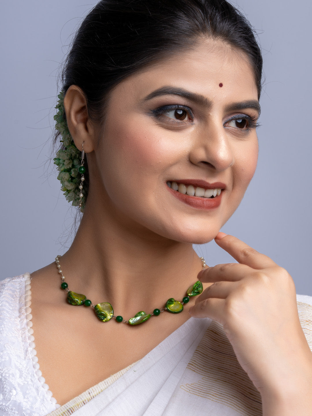 Handmade mother of pearl necklace set with green accents worn by smiling woman in white attire