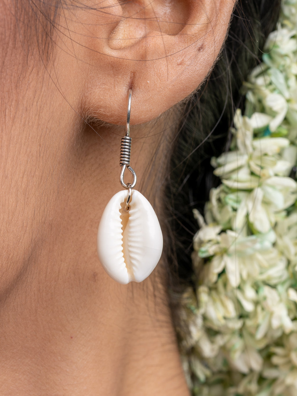 Handmade cowrie shell earring from LOOK AND ADORN necklace set worn on ear with floral background