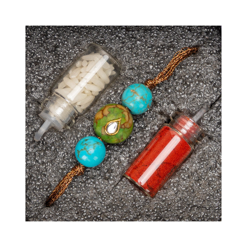 Kundan rakhi with blue and green beads alongside red and white decorative powders from LOOK AND ADORN