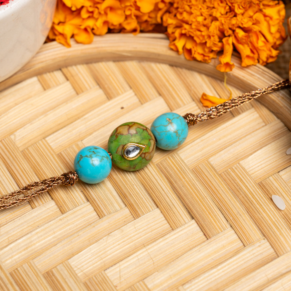 LOOK AND ADORN kundan rakhi with turquoise and green beads on a woven bamboo tray with marigold flowers