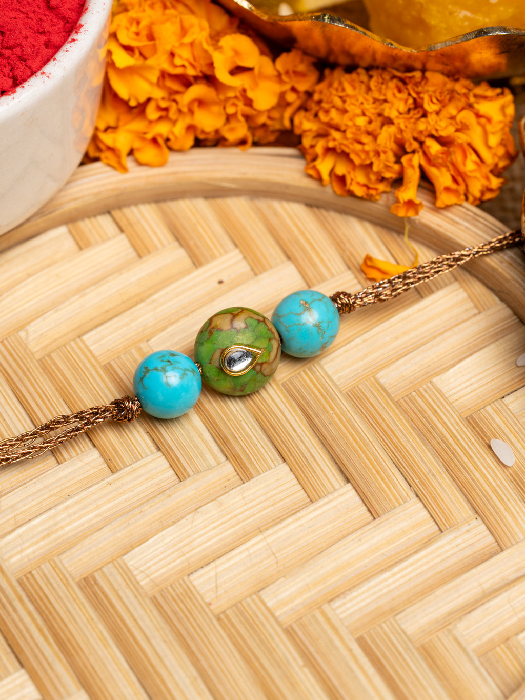 LOOK AND ADORN kundan rakhi with turquoise and green beads on a woven bamboo tray with marigold flowers