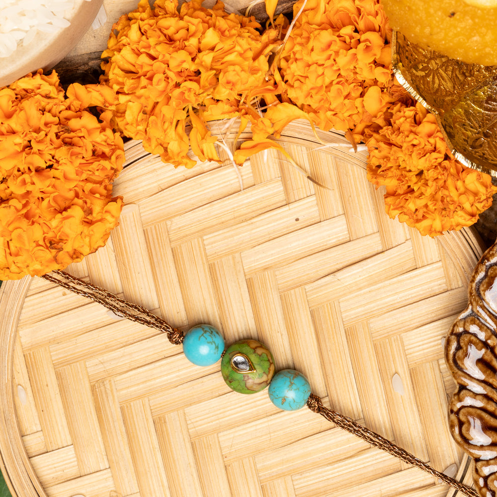 Kundan rakhi with blue and green beads on a traditional bamboo plate surrounded by marigold flowers and festive items
