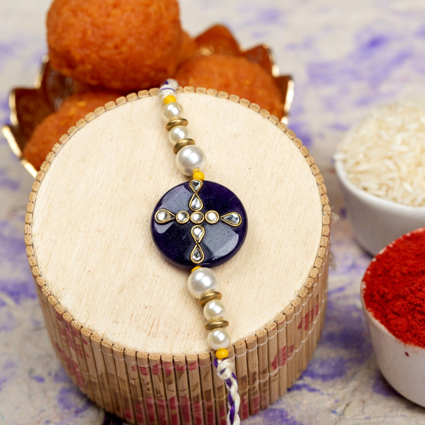 LOOK AND ADORN kundan rakhi with pearl and gold bead detailing on wooden display with traditional sweets and rice