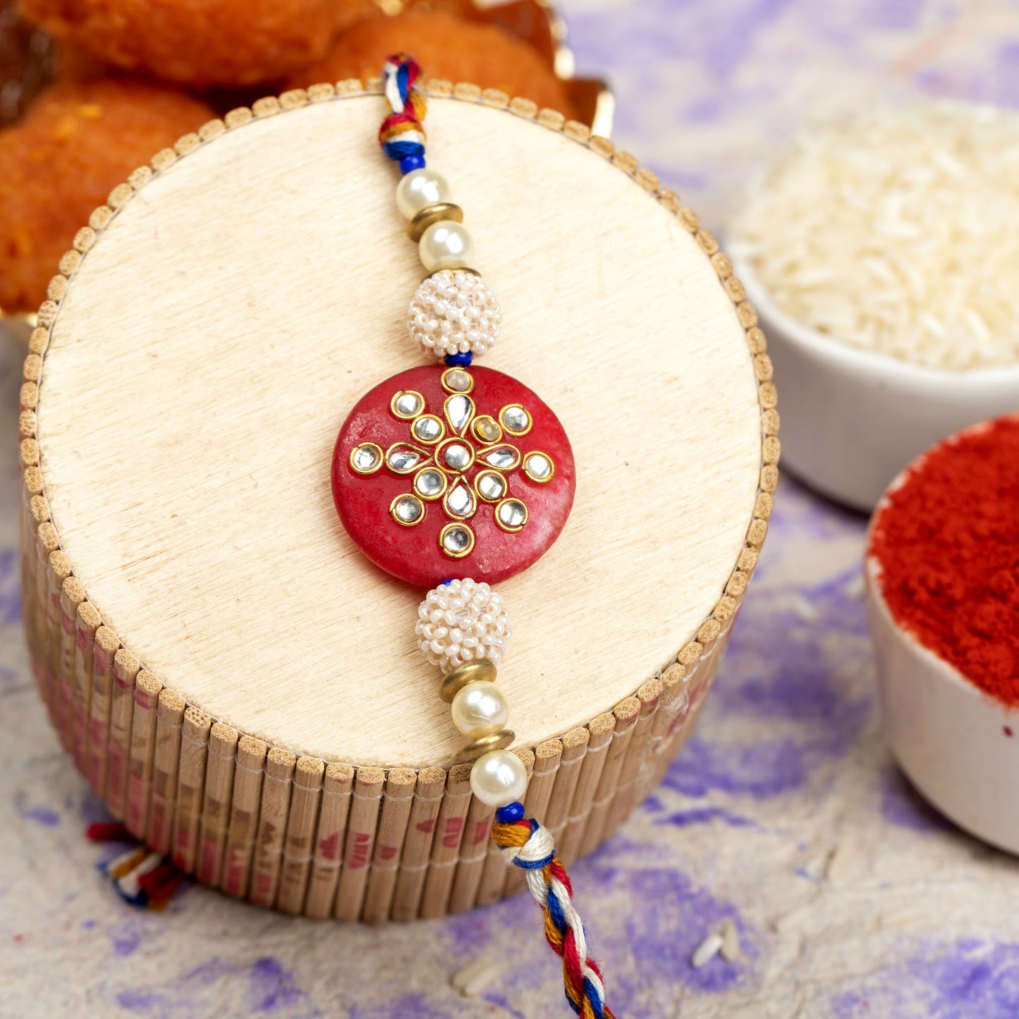 LOOK AND ADORN red and pearl studded kundan rakhi with intricate design on beige wooden surface