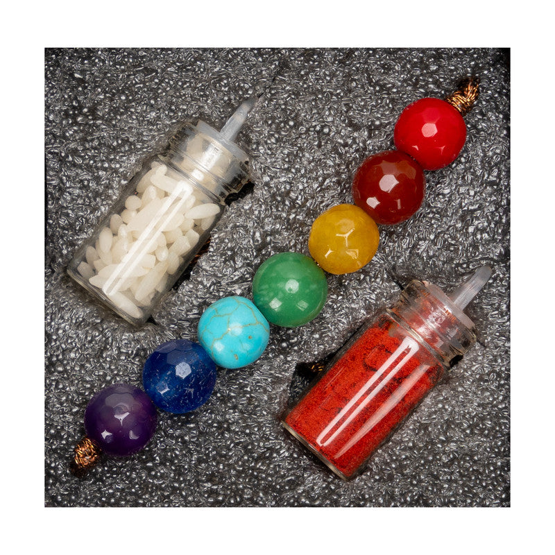 7 chakra rakhi with multicolored beads and two small spice containers on textured background