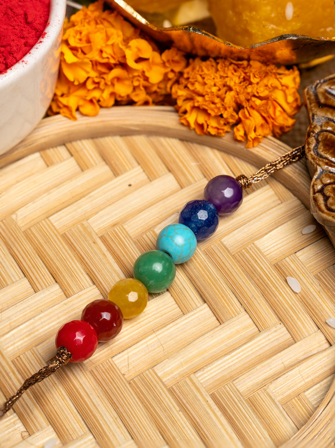LOOK AND ADORN 7 chakra rakhi with colorful gemstone beads on a woven bamboo mat