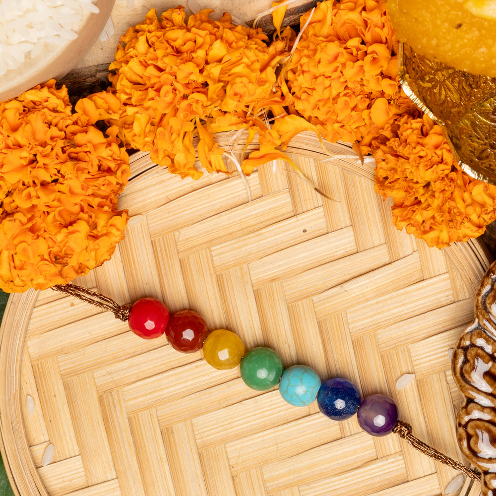 7 chakra rakhi with colorful beads surrounded by marigold flowers and traditional Rakhi ceremony items
