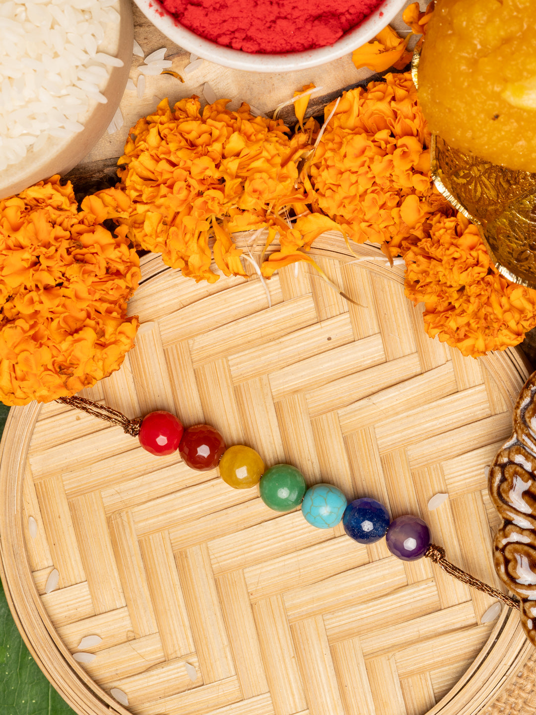 7 chakra rakhi with colorful beads surrounded by marigold flowers and traditional Rakhi ceremony items