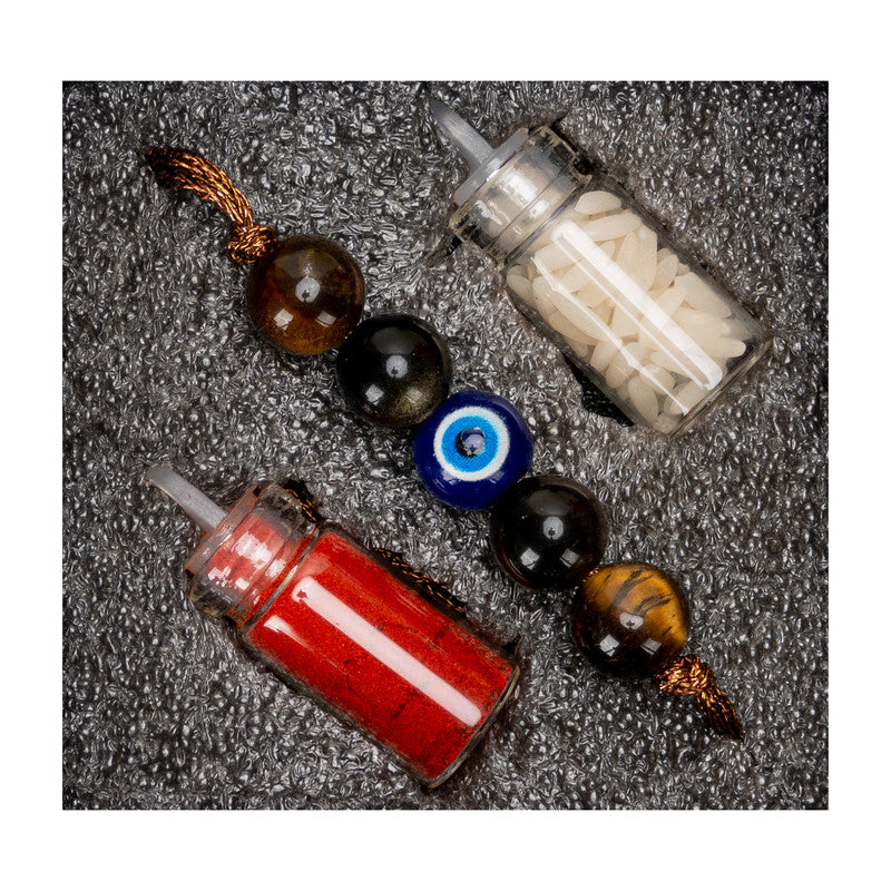 LOOK AND ADORN evil eye rakhi with beads and small bottles of red and white powder on textured background