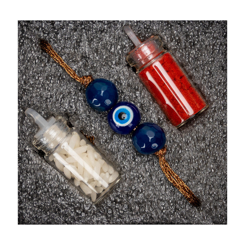 Evil eye rakhi with blue beads and small containers of red and white powders by LOOK AND ADORN