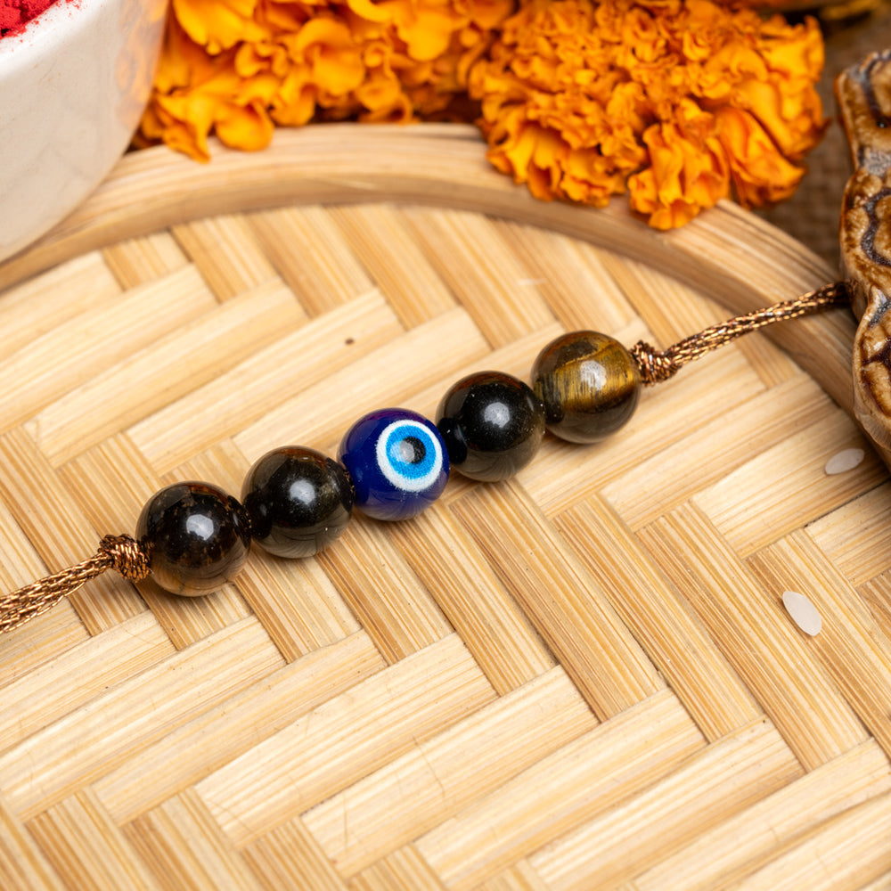LOOK AND ADORN evil eye rakhi with black and blue beads on a woven wooden surface with marigold flowers
