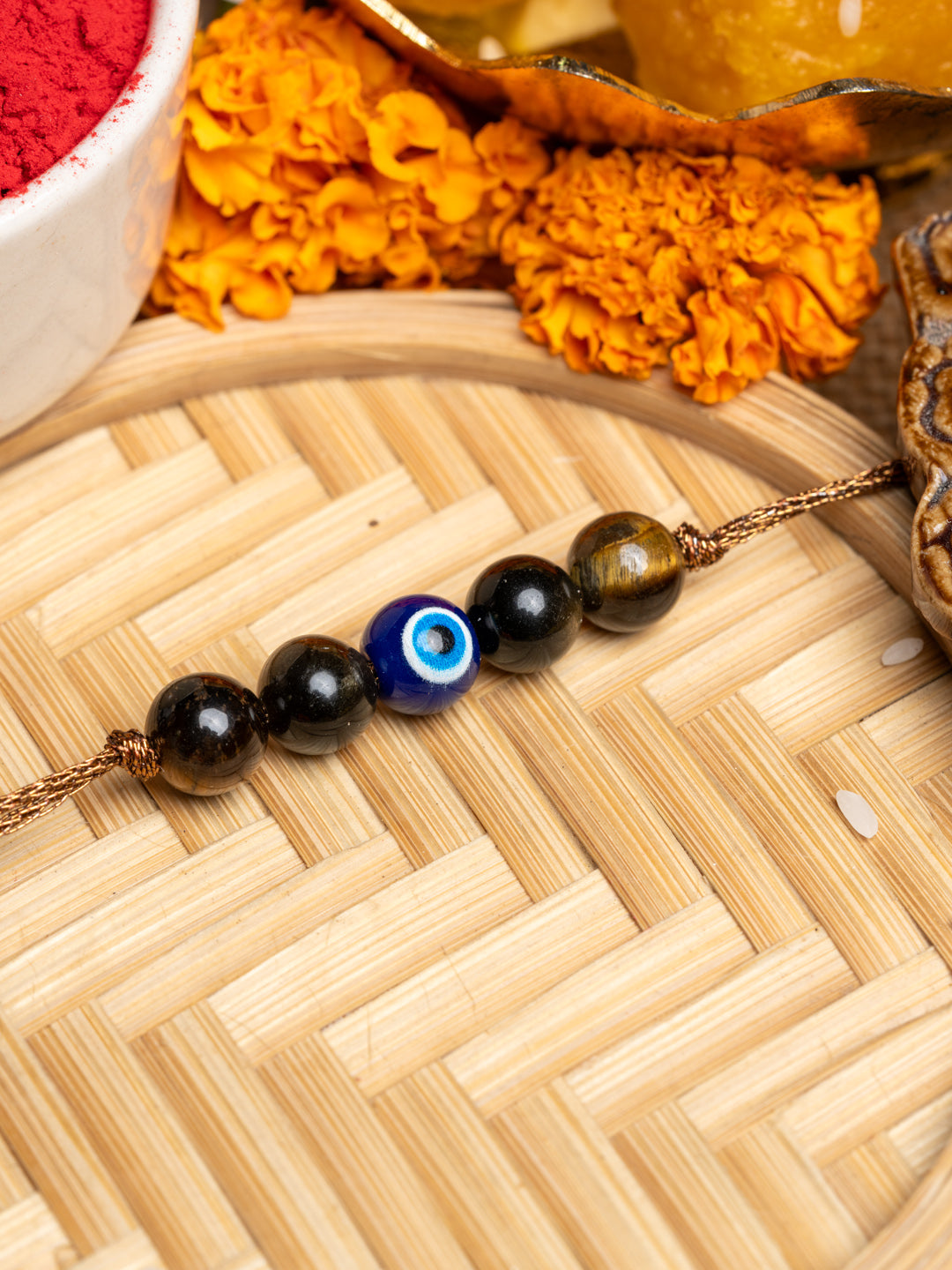 LOOK AND ADORN evil eye rakhi with black and blue beads on a woven wooden surface with marigold flowers
