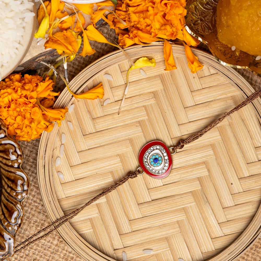 LOOK AND ADORN evil eye rakhi with blue and white beads on a woven tray surrounded by marigold flowers and traditional items