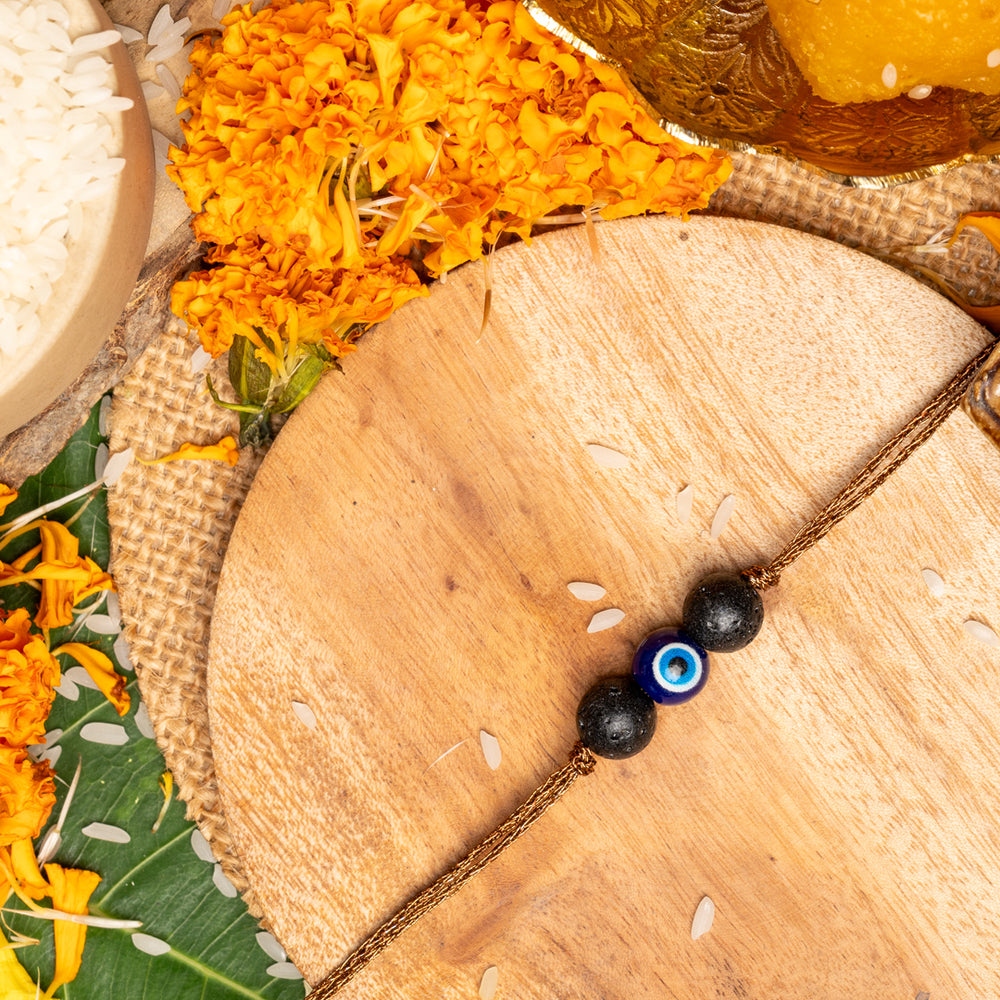 LOOK AND ADORN evil eye rakhi with blue and black beads on wooden plate with marigold flowers and traditional pooja items
