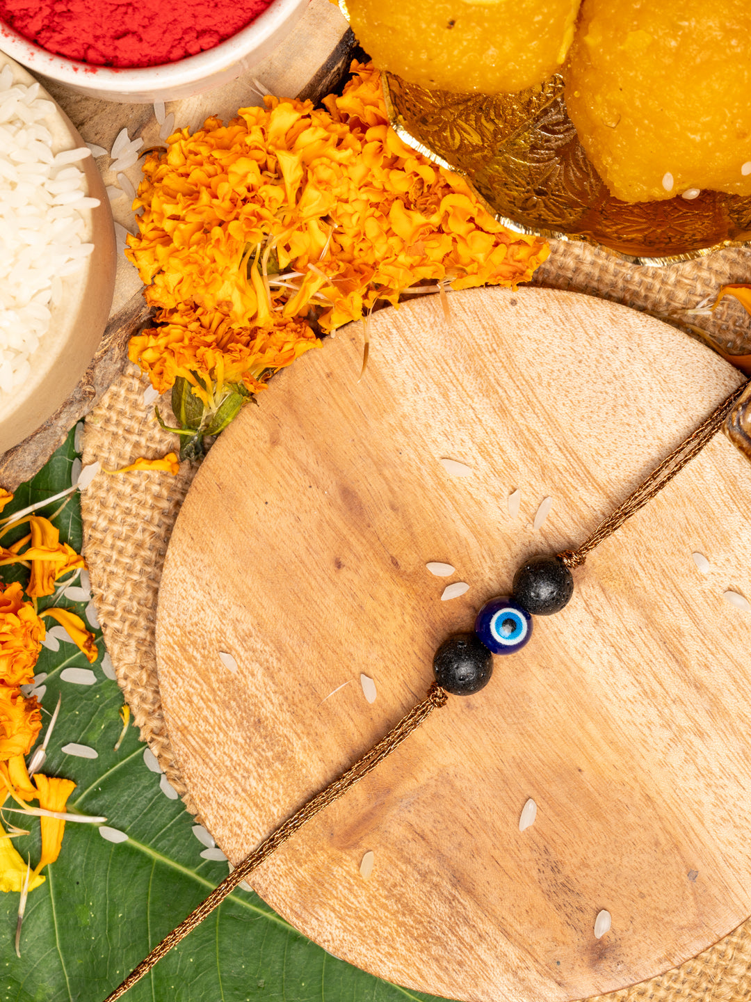 LOOK AND ADORN evil eye rakhi with blue and black beads on wooden plate with marigold flowers and traditional pooja items