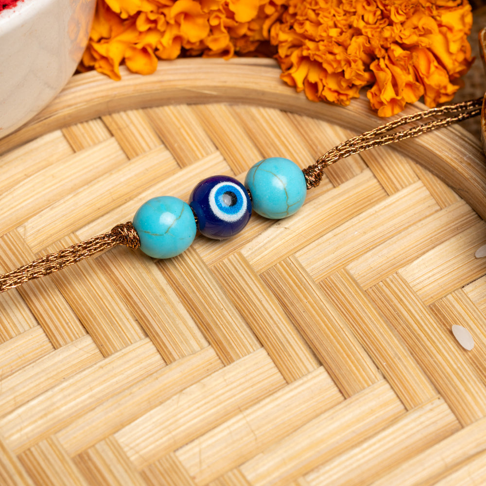 LOOK AND ADORN evil eye rakhi with blue and turquoise beads on a golden thread with marigold flowers