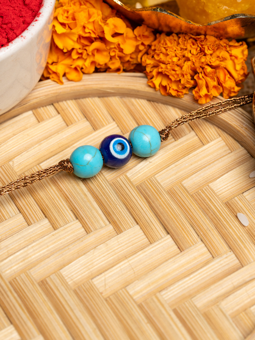 LOOK AND ADORN evil eye rakhi with blue and turquoise beads on a golden thread with marigold flowers