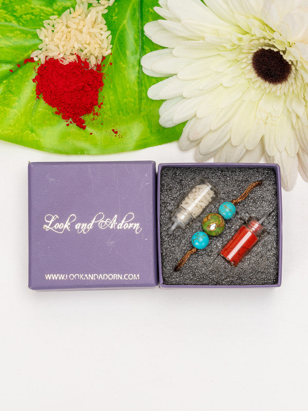 LOOK AND ADORN kundan rakhi with decorative beads in a purple gift box beside white flower and colorful powders