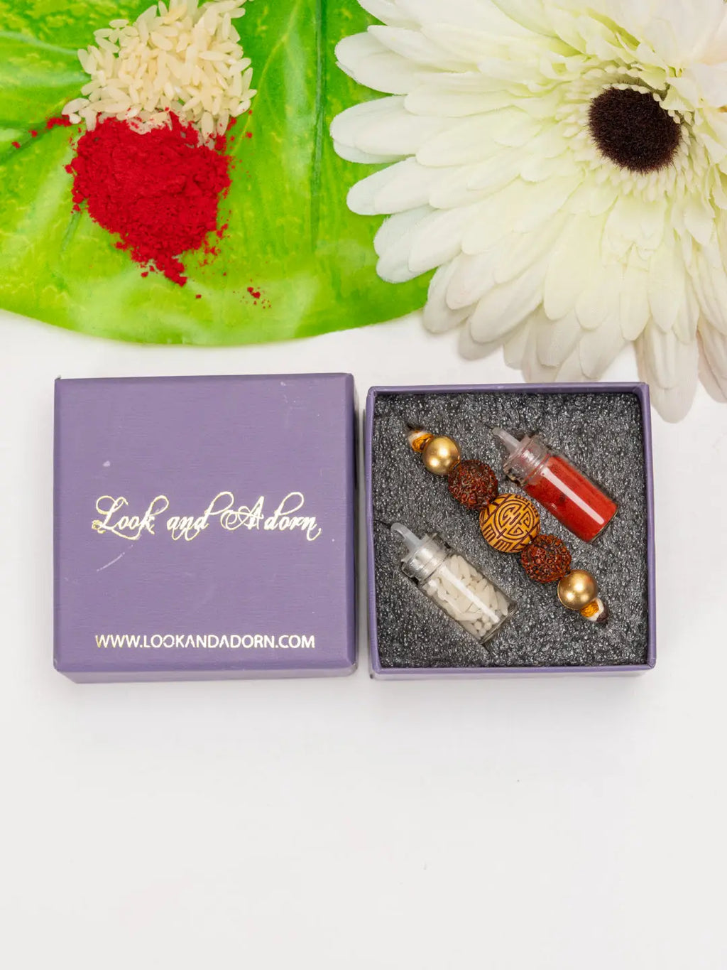 Rudraksh rakhi set by LOOK AND ADORN in a purple gift box with red and white powders and white flower