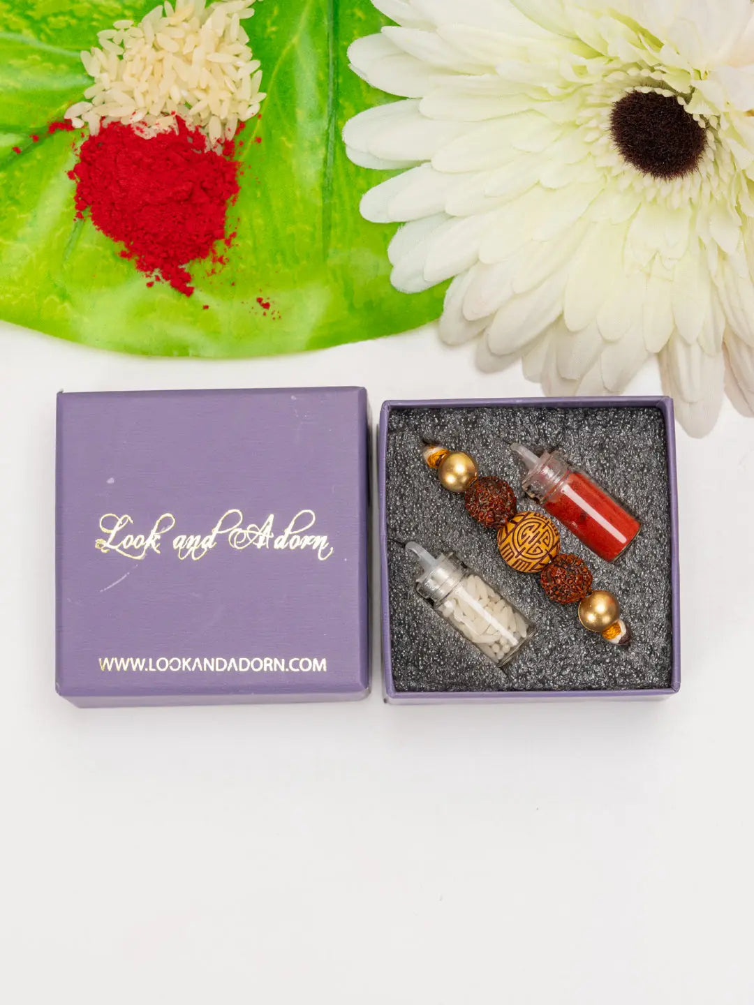Rudraksh rakhi set by LOOK AND ADORN in a purple gift box with red and white powders and white flower