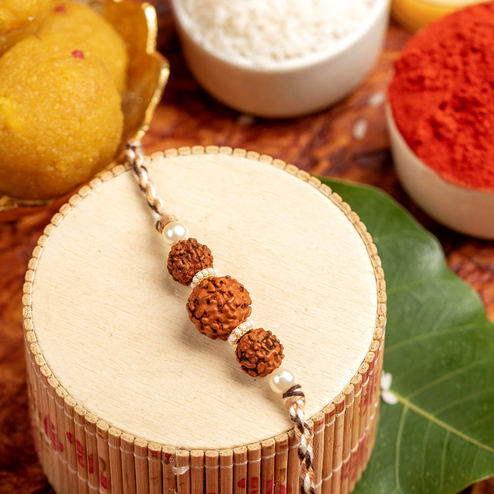 LOOK AND ADORN rudraksh rakhi with three rudraksh beads and pearls on decorative wooden stand