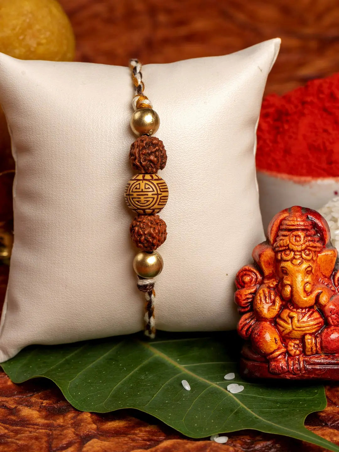 LOOK AND ADORN rudraksh rakhi with gold beads displayed on cushion next to Ganesh idol and traditional decorations