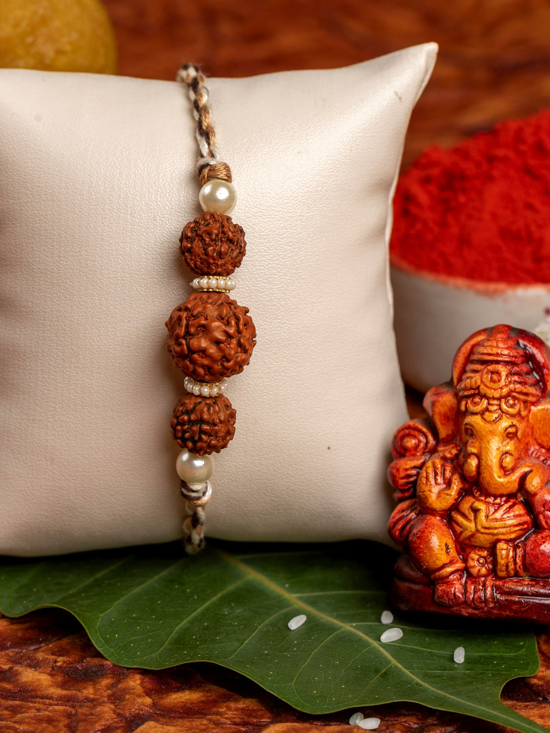 LOOK AND ADORN rudraksh rakhi with three beads and pearl accents displayed on a white cushion next to a small Ganesha idol