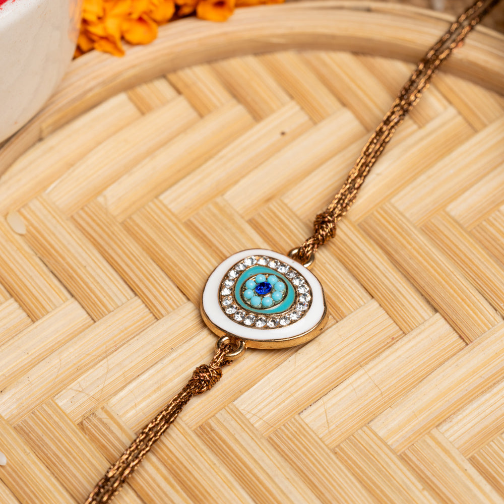 LOOK AND ADORN evil eye rakhi with blue and white stones on a braided thread on wooden surface
