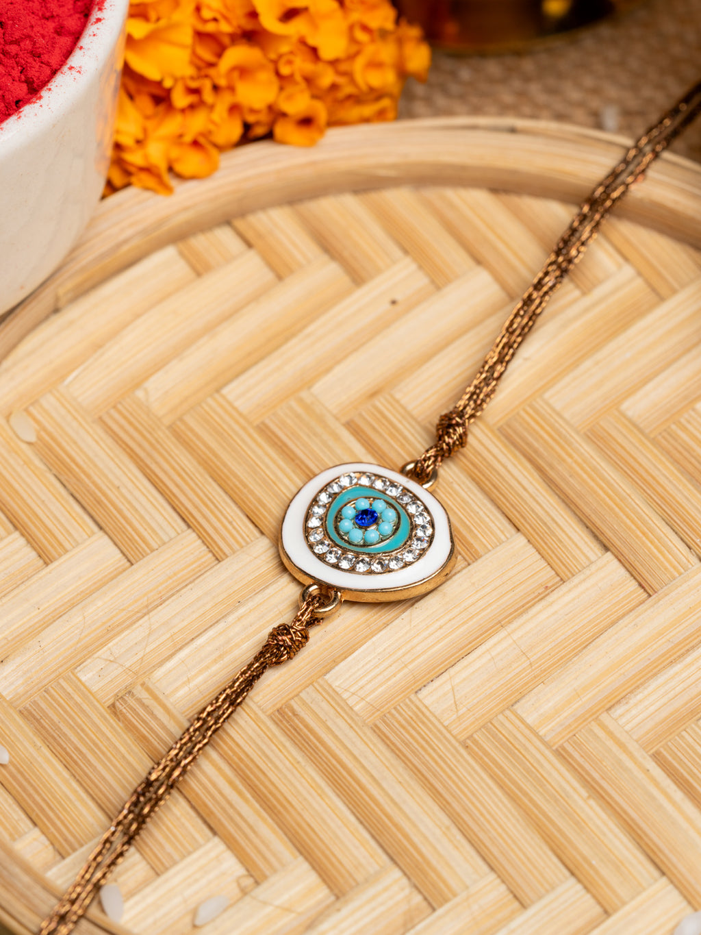 LOOK AND ADORN evil eye rakhi with blue and white stones on a braided thread on wooden surface
