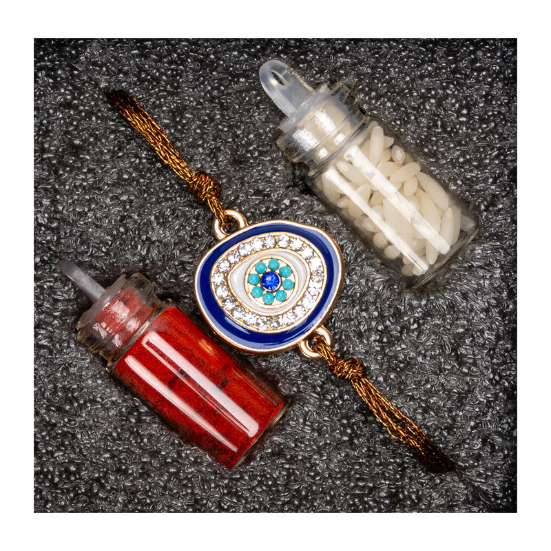 LOOK AND ADORN evil eye rakhi with blue and gold design alongside red and white ritual items on textured surface