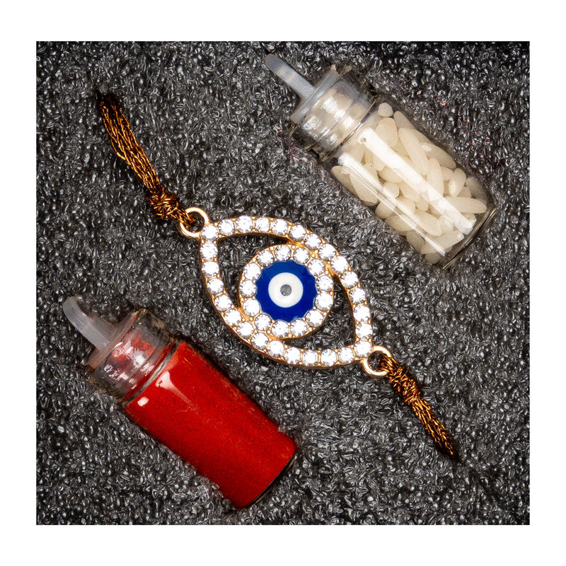Diamond-studded evil eye rakhi with blue center and golden thread alongside red and white ritual powders