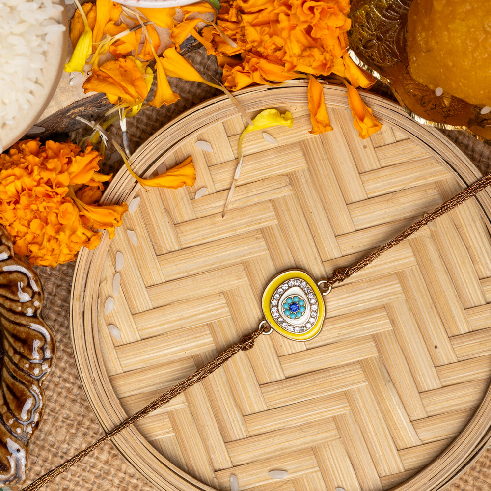 LOOK AND ADORN evil eye rakhi with blue and white stones on wooden plate with marigold flowers and traditional puja items