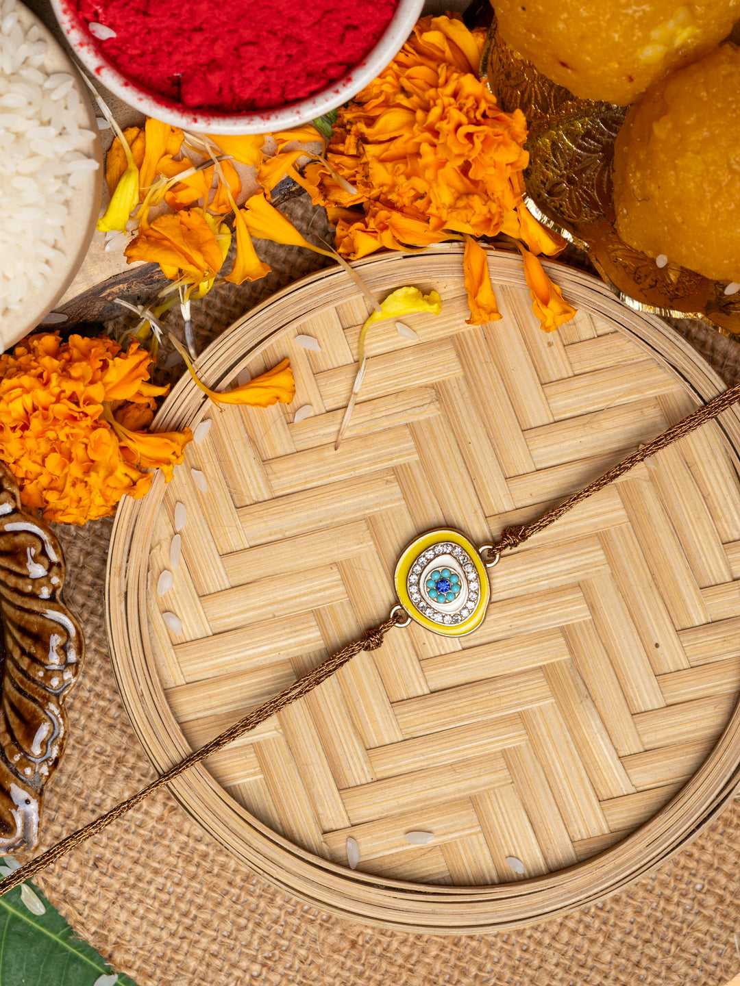 LOOK AND ADORN evil eye rakhi with blue and white stones on wooden plate with marigold flowers and traditional puja items