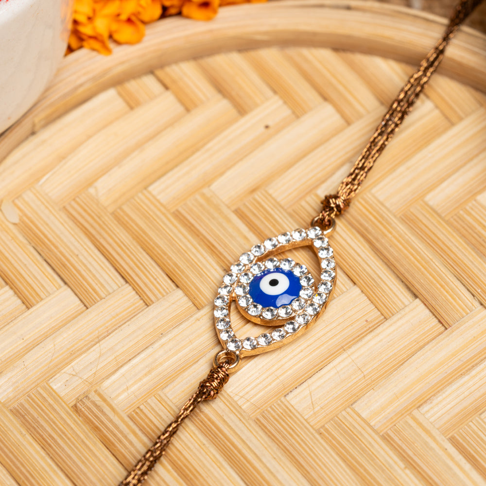 LOOK AND ADORN evil eye rakhi with blue center and crystal-studded design on golden thread