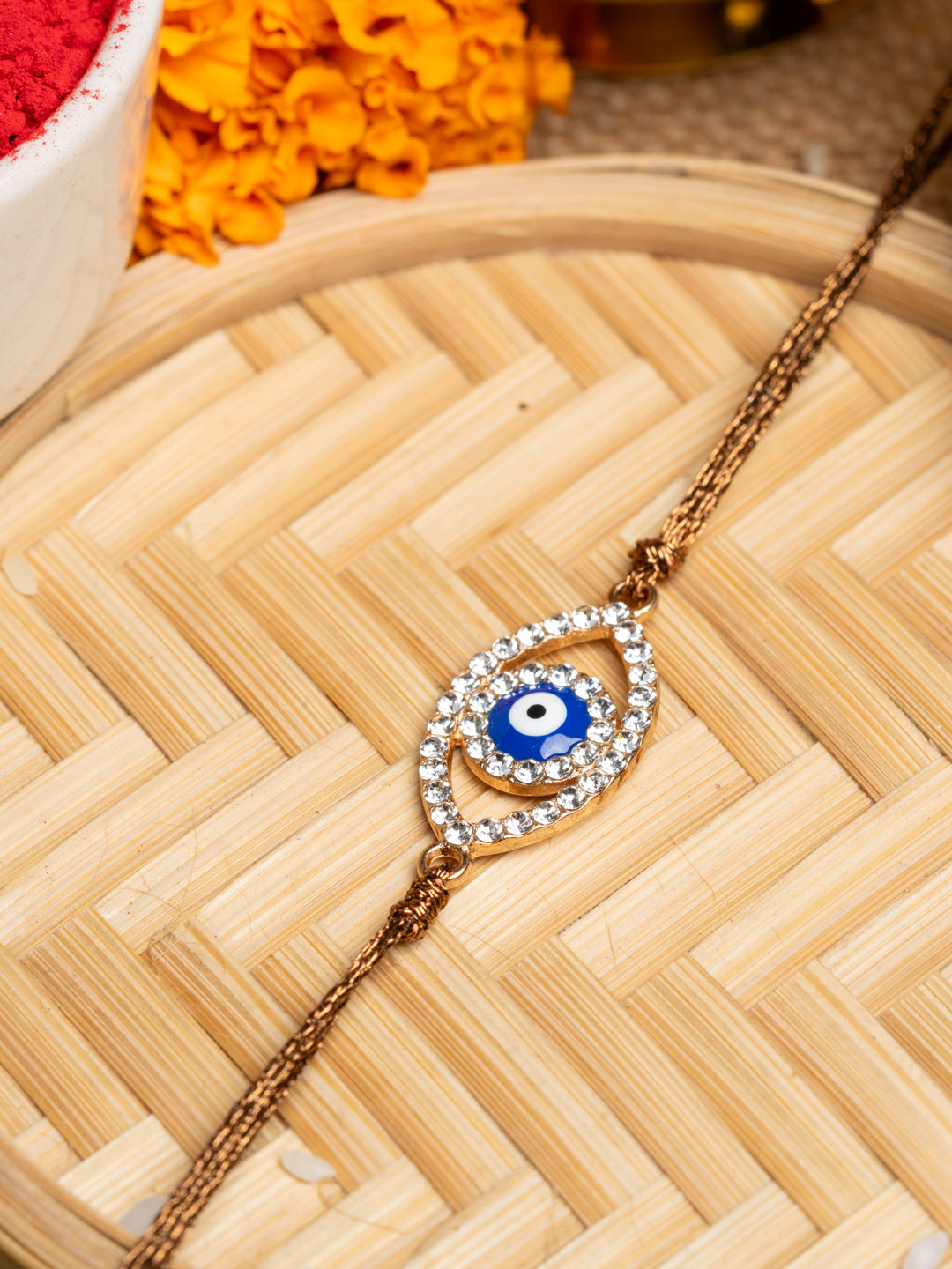 LOOK AND ADORN evil eye rakhi with blue center and crystal-studded design on golden thread