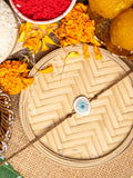 LOOK AND ADORN evil eye rakhi with blue and white charm on a woven tray surrounded by marigold flowers and traditional pooja items