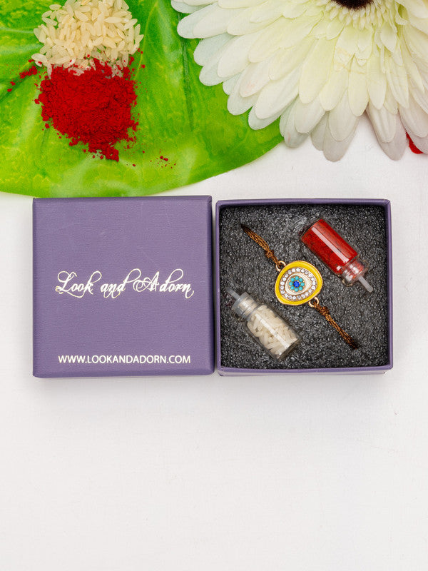 LOOK AND ADORN evil eye rakhi in a purple gift box with decorative rice and flower accents