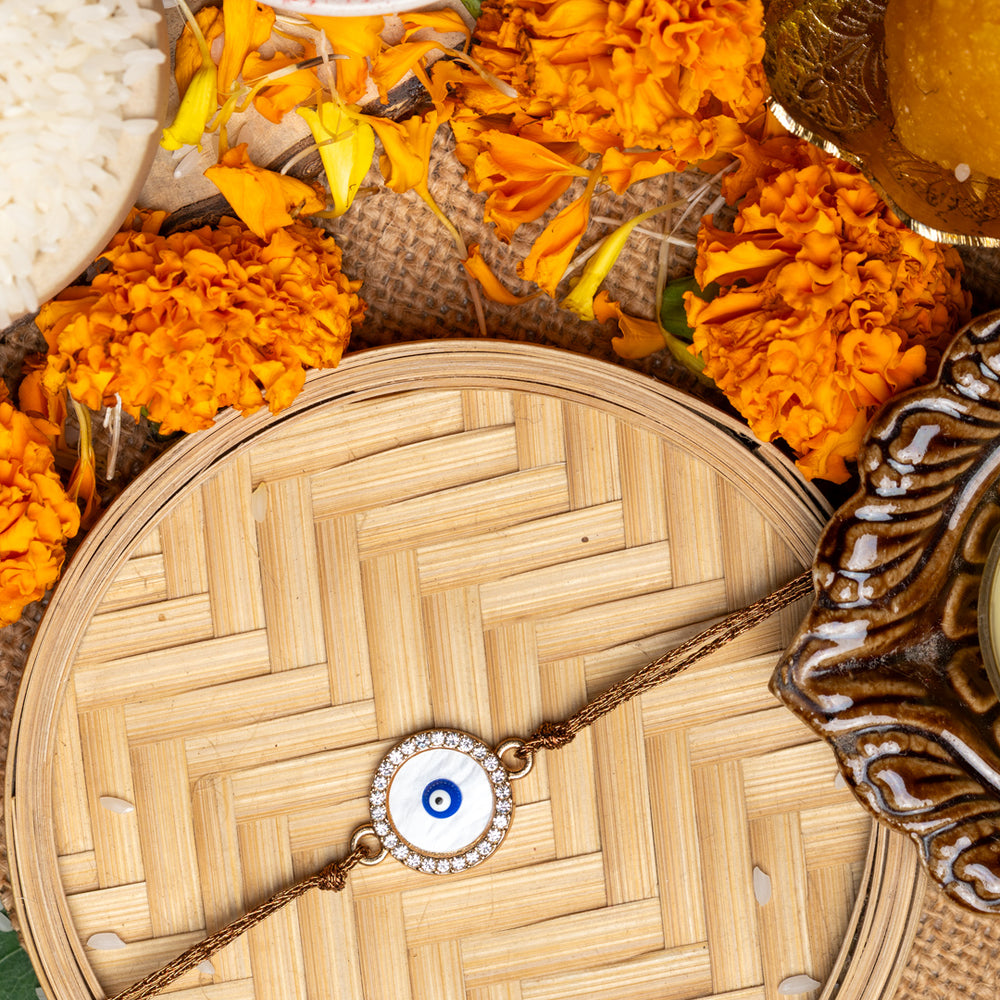 LOOK AND ADORN evil eye rakhi on woven tray surrounded by marigold flowers and traditional puja items