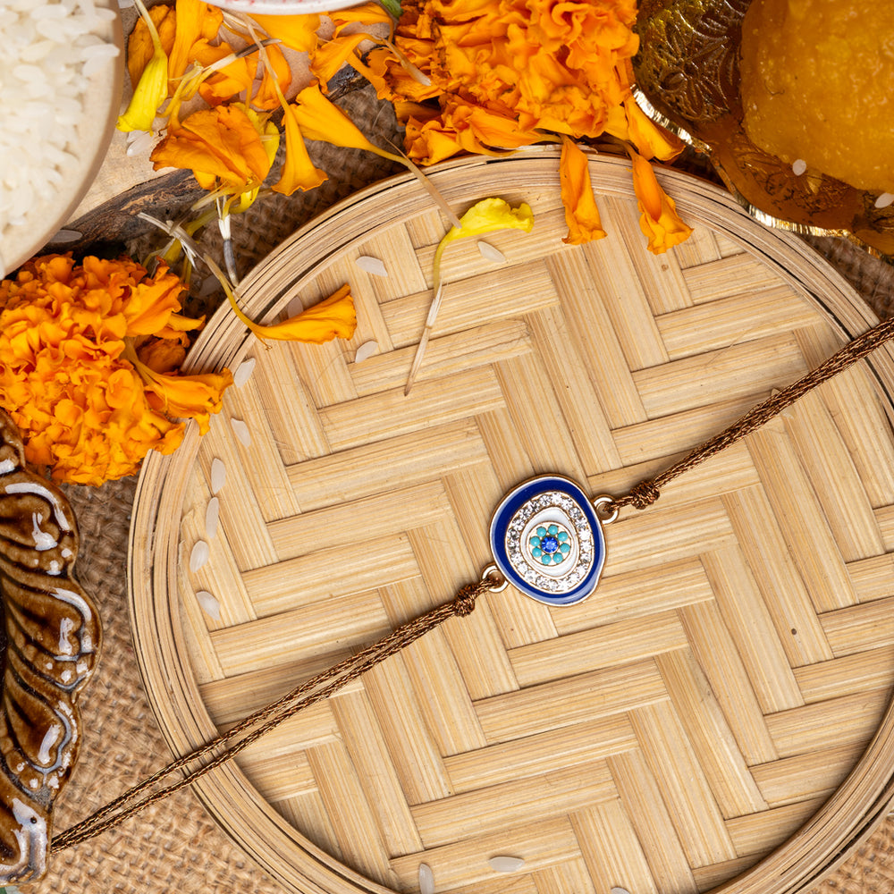 LOOK AND ADORN evil eye rakhi with blue and white charm on a woven plate with marigold flowers and traditional pooja items