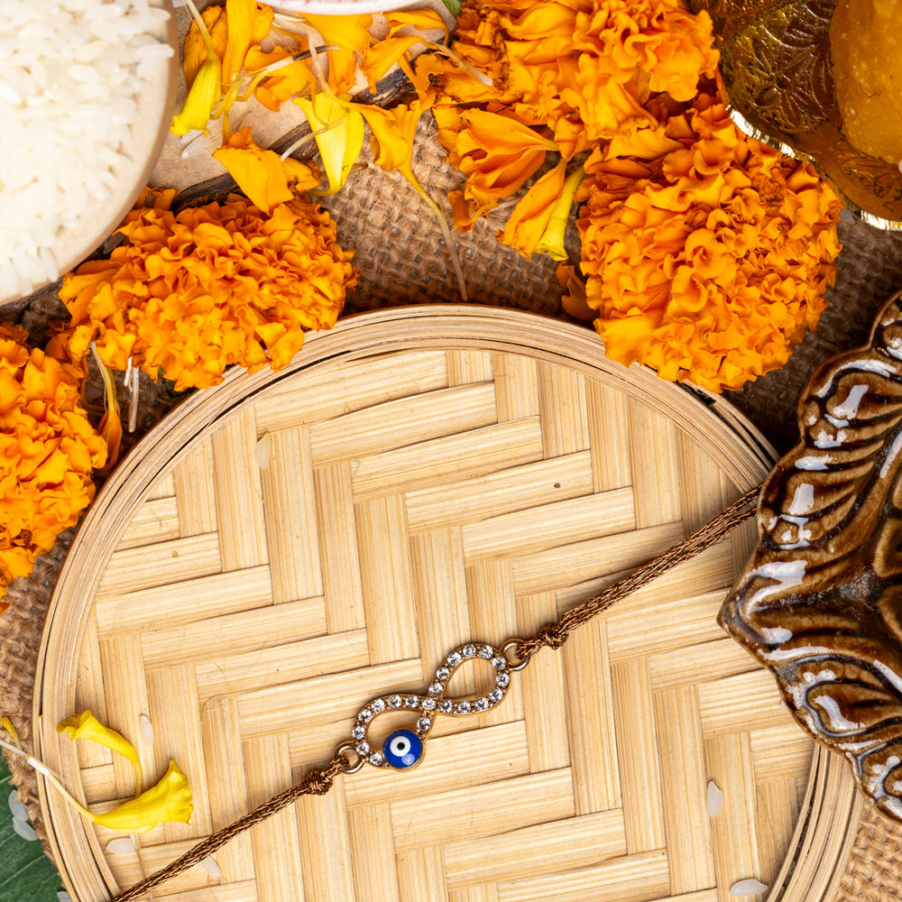 Evil eye rakhi on a woven bamboo plate surrounded by marigold flowers and traditional ritual items