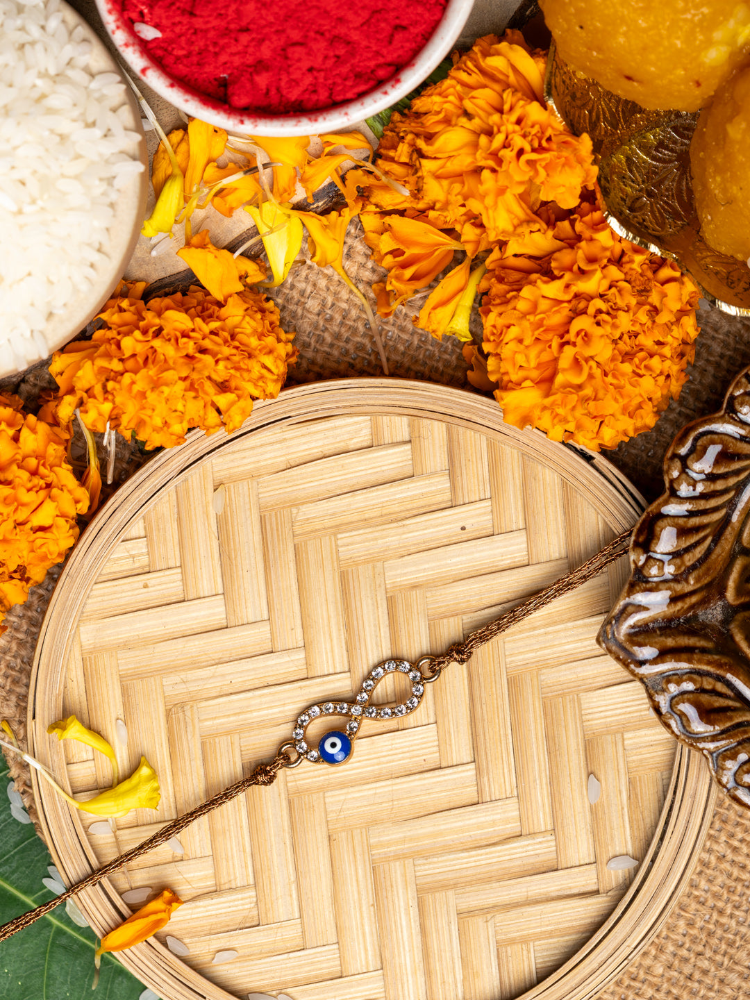 Evil eye rakhi on a woven bamboo plate surrounded by marigold flowers and traditional ritual items