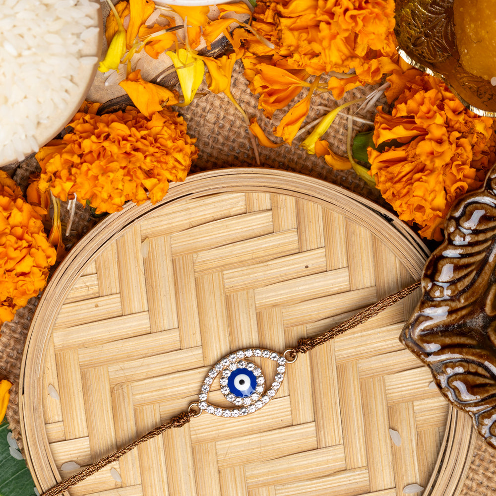 LOOK AND ADORN evil eye rakhi with blue and white bead design surrounded by marigold flowers and traditional pooja items