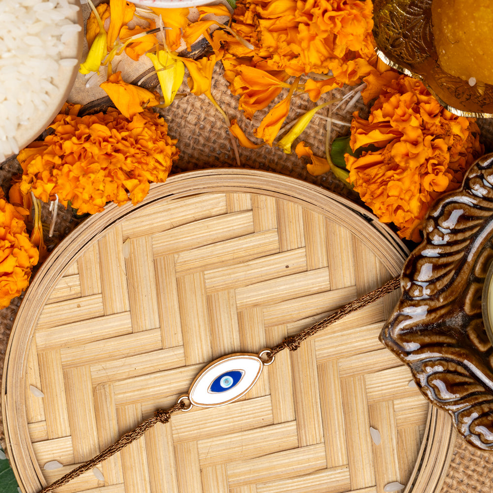 LOOK AND ADORN evil eye rakhi with blue eye charm on a woven bamboo plate surrounded by marigold flowers and traditional pooja items