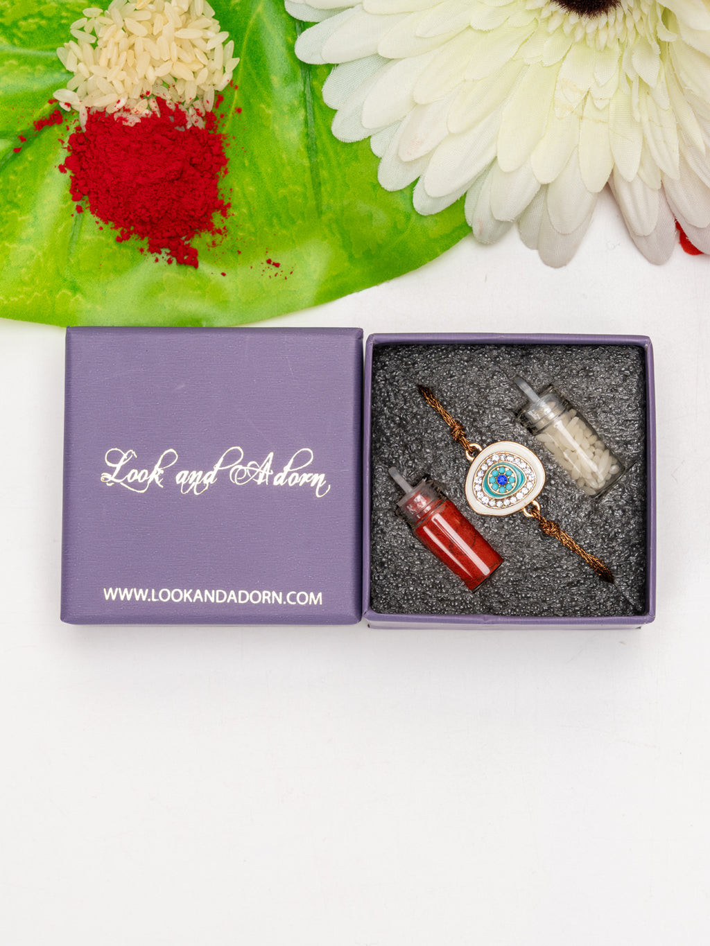 Evil eye rakhi with blue and white charm in a purple Look and Adorn box with red and white powder