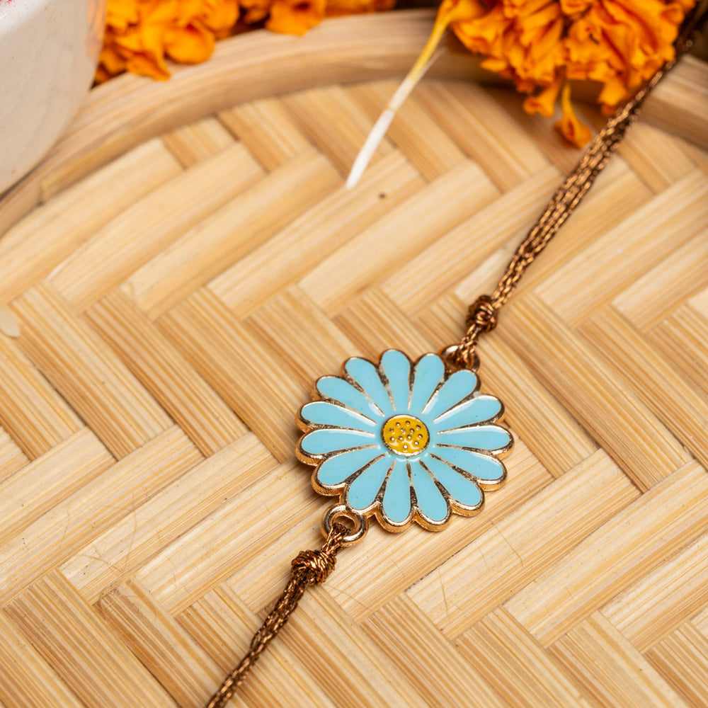 LOOK AND ADORN floral rakhi with blue petals and yellow center on a woven bamboo background
